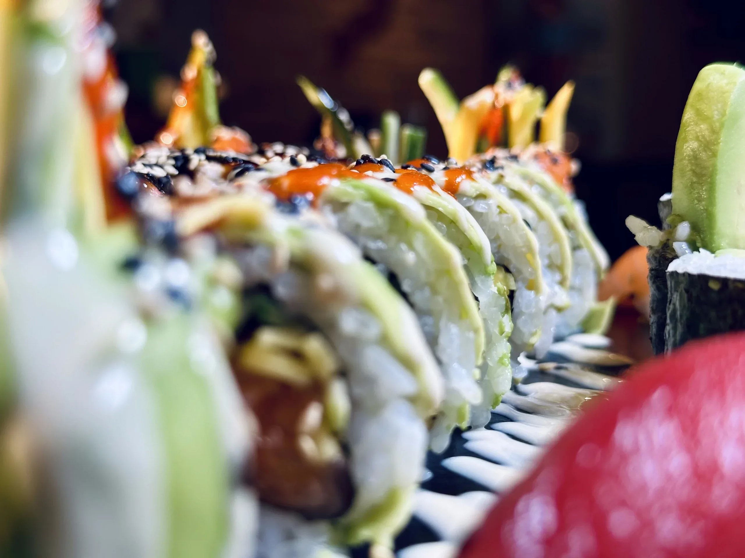 Nahaufnahme von Sushi-Rolls mit Avocado, Sesam und roter Sauce auf einem Servierteller.