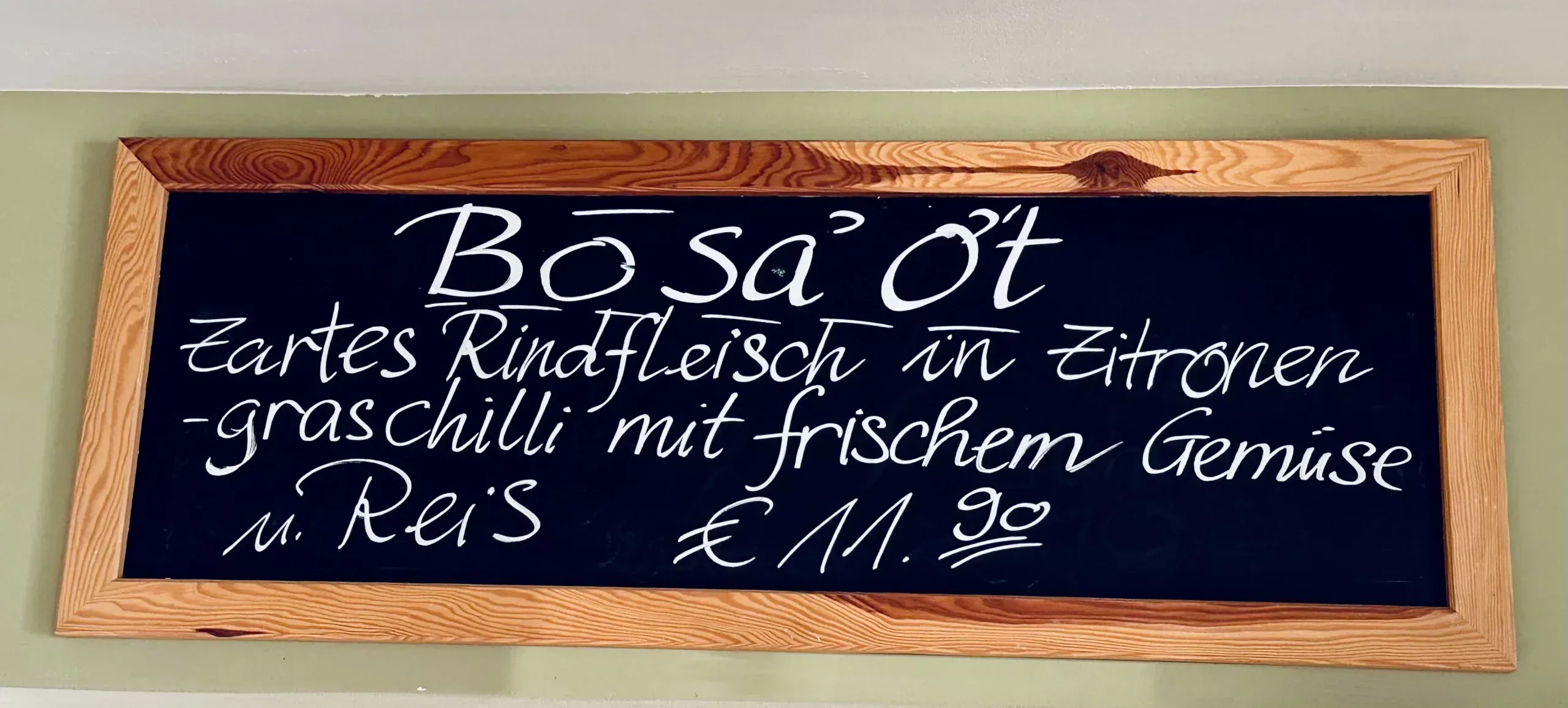 Schwarze Kreidetafel mit Tagesgericht „Bò Sá Ớt“: Rindfleisch in Zitronengras-Chili mit frischem Gemüse und Reis, Preis 11,90 €.