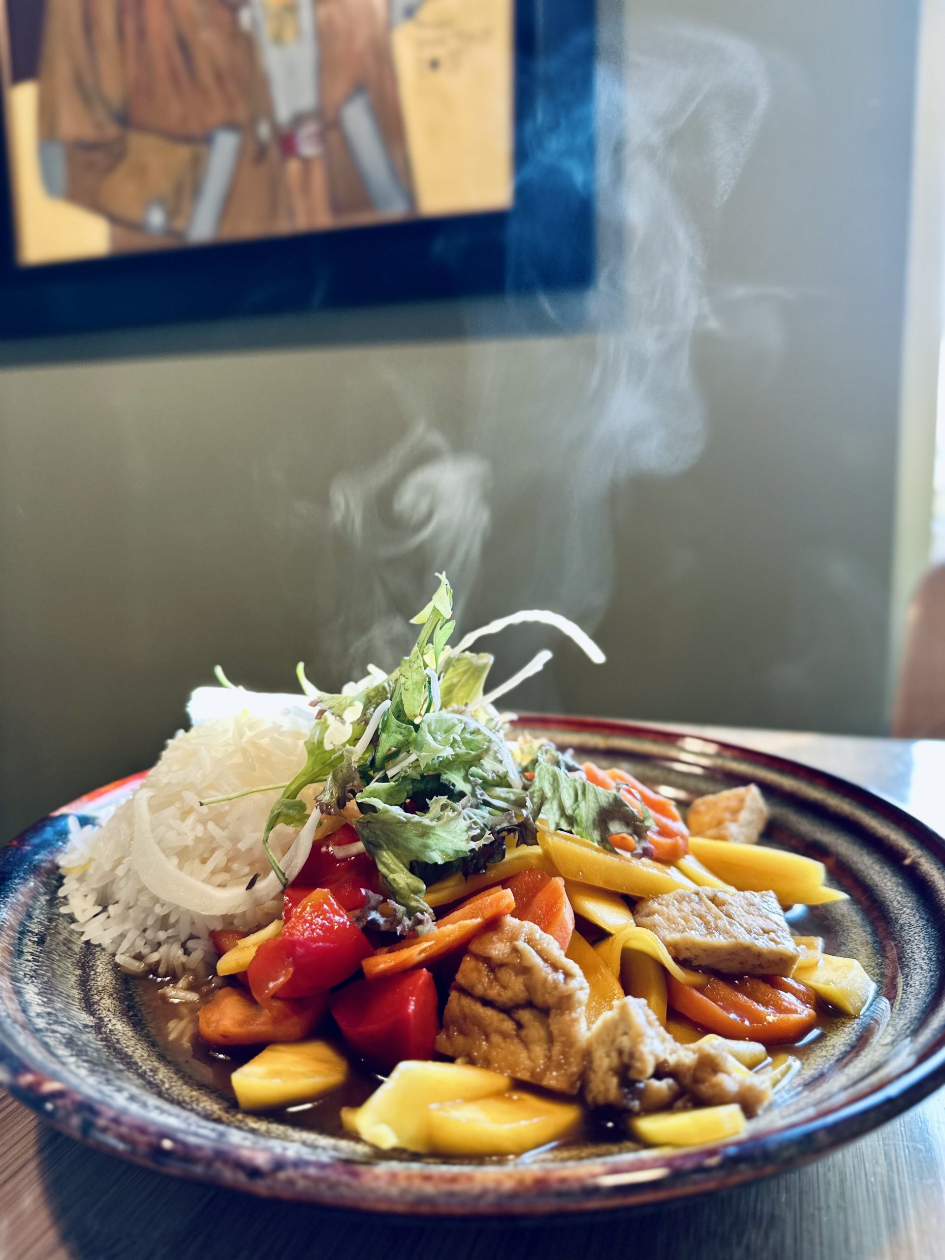 Dampfender Teller mit Reis, Mango, Gemüse und Kräutern in Sauce, angerichtet als vietnamesisches Hauptgericht.