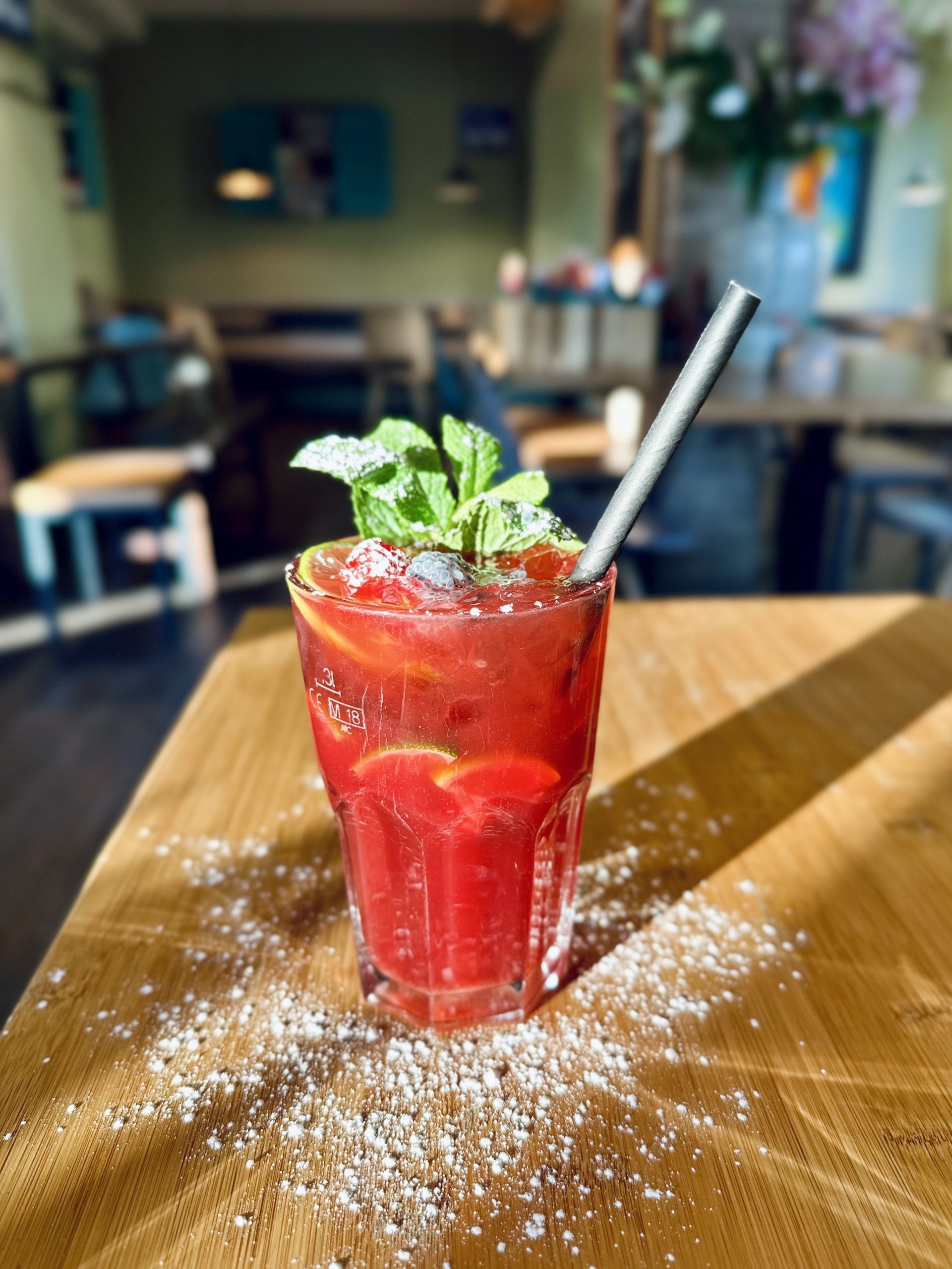 Roter Cocktail mit Eis, Minze und Zitrus-Scheiben im Glas auf einem Holztisch im Restaurant.