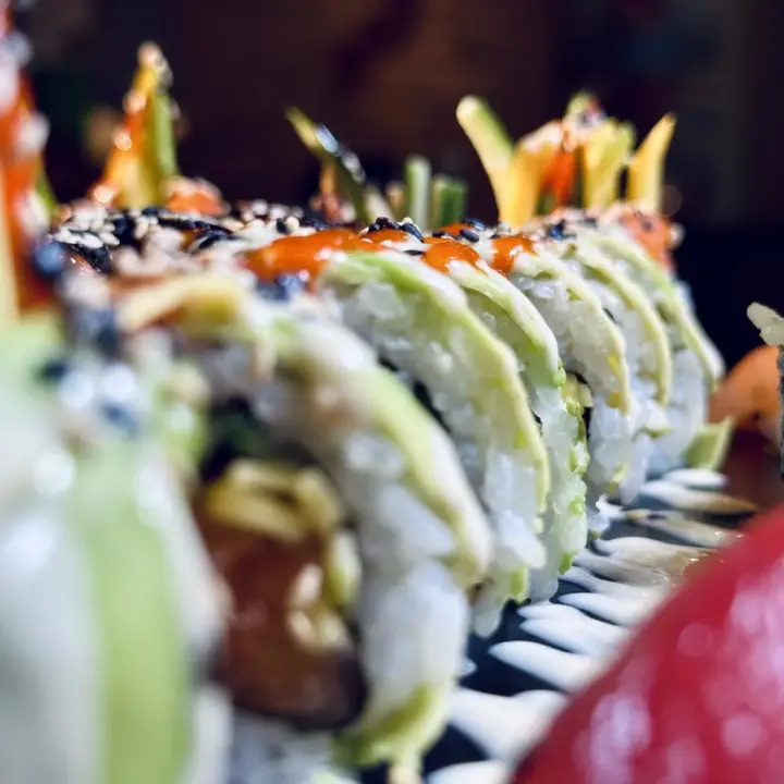 Nahaufnahme von Sushi-Rolls mit Avocado, Sesam und roter Sauce auf einem Servierteller.