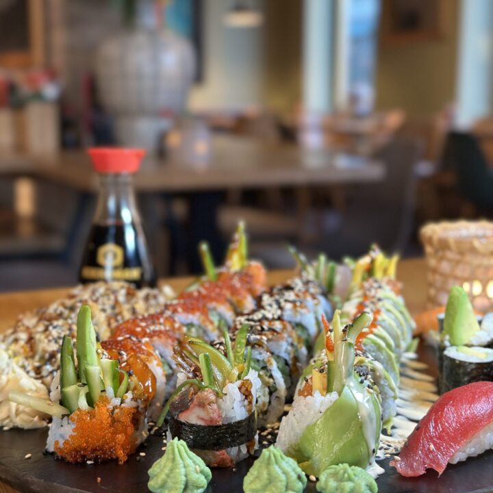 Sushi-Platte mit verschiedenen Rolls, Nigiri, Wasabi und Sojasauce-Flasche im Hintergrund auf einem Restauranttisch.