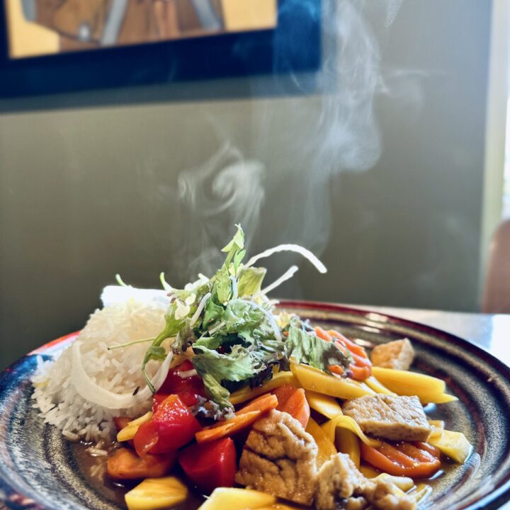 Dampfender Teller mit Reis, Mango, Gemüse und Kräutern in Sauce, angerichtet als vietnamesisches Hauptgericht.